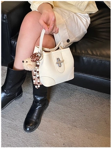 Detail of off-white bucket bag featuring silver twist lock and cute bear charm accent