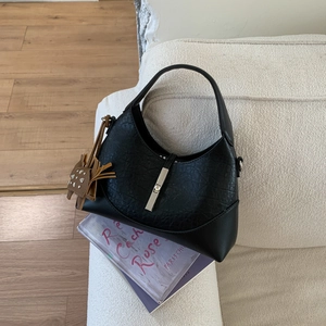 Close-up of black textured leather bag with silver metal buckle and cat tassel detail