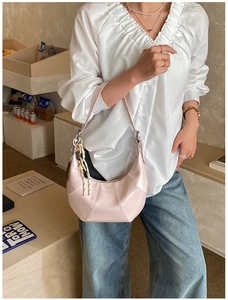 Detail view of pink leather hobo bag with woven charm and metallic buckle in soft light