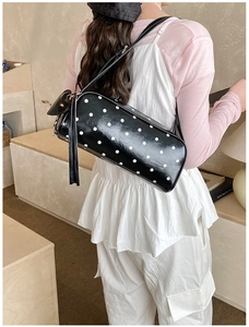 Detailed close-up of a black polka dot cylindrical handbag with long tassels and thin straps