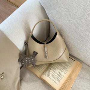 Detail of beige crescent hobo bag with silver lock and studded pony charm on sofa
