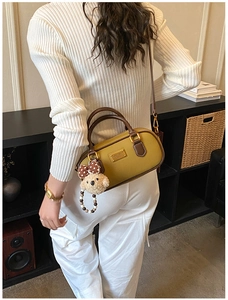 Detail of olive yellow cylinder handbag with brown handles and a cute bear charm