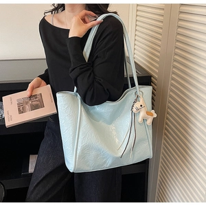 Detail view of light blue tote bag in glossy pleated leather with a horse charm accessory