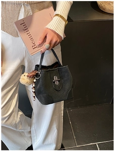 Detail of black bucket bag with matte leather texture, plush charm and vintage beads