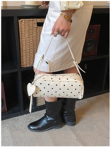 Detailed view of white polka dot shoulder bag with a heart pendant and slim handle