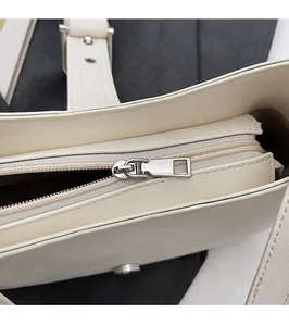 Detailed close-up of smooth silver zipper hardware on a cream leather shoulder handbag