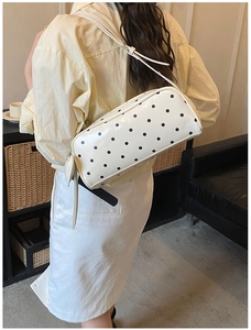 Chic cream-colored polka dot cylinder shoulder bag worn by a model in a cozy interior