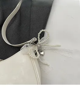 Detail of cream leather shoulder bag with pearl bow, lace ribbons and silver heart charm
