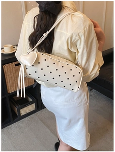 Close-up of cream polka dot underarm bag with heart pendant and long tassel details