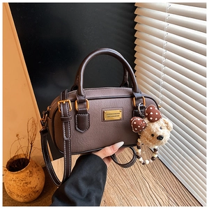 Close-up of brown pebbled leather Boston bag with gold nameplate and cute bear charm