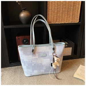 Detail of light blue pixelated tote bag featuring double handles and a beige horse charm
