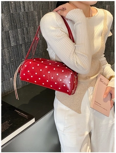 Close-up of red polka dot cylinder bag featuring a long leather zipper puller and strap