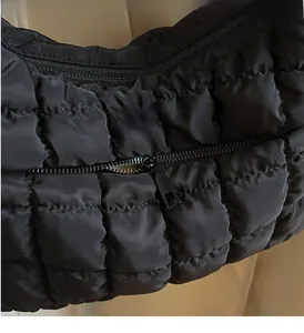 Detail of smooth black metal zipper on quilted nylon shoulder bag fabric texture