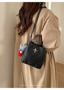 Close-up of a black lychee texture bucket bag with a gold lock and a cute bear charm