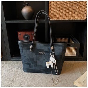 Detailed shot of dark grey bucket tote bag with leather logo and pony charm in home setting
