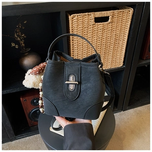Detail of black bucket bag featuring a silver twist lock and a cute plush bear charm
