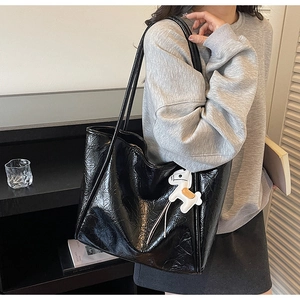 Detail of black large tote bag with wrinkled texture and white horse charm accessory