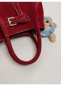 Detailed close-up of dark red leather bag handle with metal buckle and plush bear charm