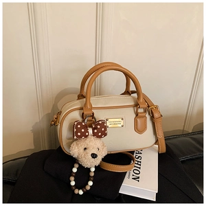 Detail of beige Boston bag featuring a brown trim and a cute plush dog pendant charm
