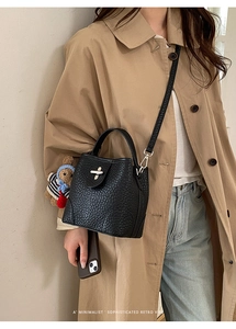 Litchi pattern bucket bag with bear charm shown in a minimalist crossbody styling