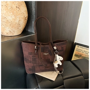 Detail of a dark brown textured tote bag with leather tag and white pony charm