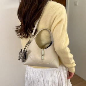 Model wearing a cream shoulder bag with cat charm and metal buckle detail
