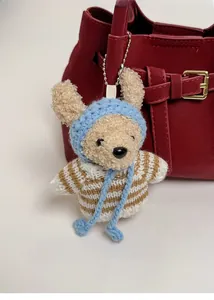 Close-up of cute plush bear charm with striped sweater and blue hat on leather bag