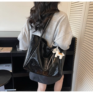 Detail of a large black glossy tote bag with a white horse charm in a modern setting