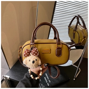 Detail of yellow boston bag with teddy bear charm and gold logo plate via mirror reflection
