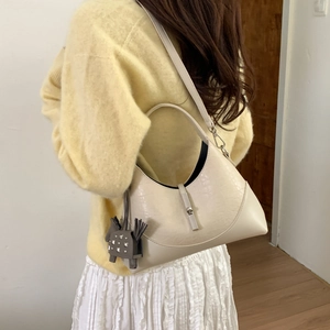 Detail of a beige crescent leather shoulder bag with a gray horse charm and metal buckle