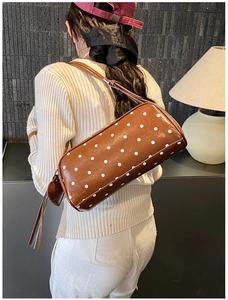 Detailed back view of a brown polka dot cylindrical bag with a heart charm on a model