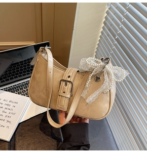 Close-up of beige shoulder bag with metal buckle and pearl lace heart charms