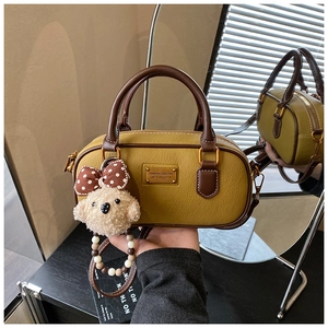 Detail of mustard yellow Boston bag with lychee texture and cute plush poodle charm