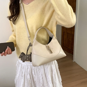 Detail view of a cream hobo bag with gold piston closure worn on a beige knit sweater