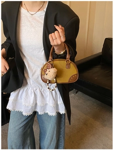 Detail of green and brown contrast leather bag with gold rivets and cute bear pendant