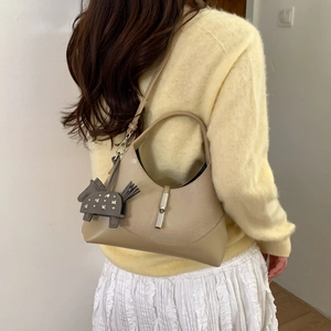 Detail of beige shoulder bag with silver clasp and small horse charm on the strap