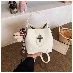 Detailed view of white bucket bag featuring a metal twist lock and cute plush puppy charm