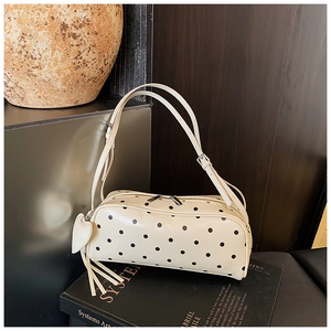 Detailed view of cream polka dot underarm bag with leather heart charm and long tassels
