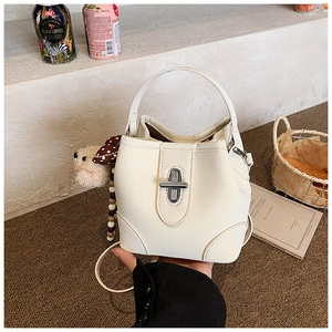 Detail of white bucket bag featuring silver turn-lock clasp and plush bear charm
