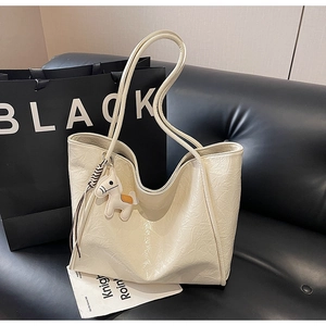 Detail of a large cream tote bag with wrinkled texture and a leather horse charm