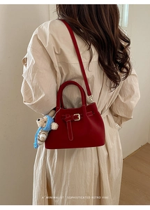 Detail of red retro crossbody bucket bag with bear charm shown on model in soft lighting