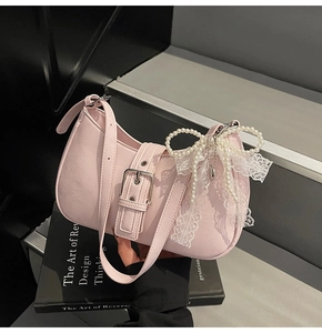 Detail of light pink PU leather bag with white lace and pearl bow charm on a book
