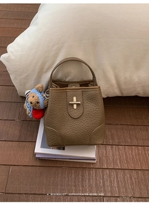 Close-up of brown pebbled leather bucket bag with cross metal lock and cute bear charm