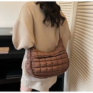 Close-up of brown quilted crescent shoulder bag with diamond stitching on a model