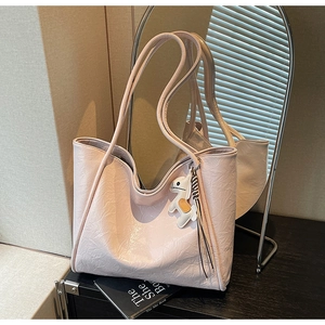 Detail of light pink crinkle leather tote bag with a decorative animal charm on black table