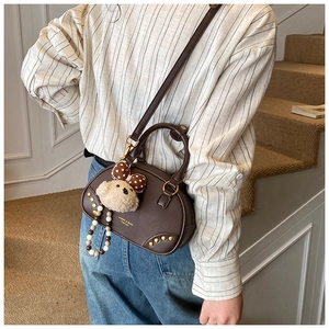 Detail view of a vintage brown leather pillow bag with gold studs and a cute bear charm