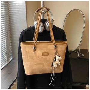 Close-up of light brown textured tote bag with a horse charm hanging on a black hoodie
