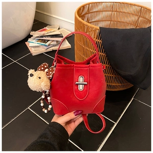 Close-up of red bucket bag featuring a gold metal twist lock and cute teddy bear charm