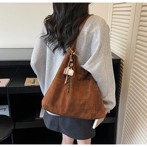 Detail of a large brown suede tote bag featuring a coffee cup charm and checkered texture
