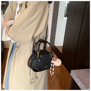 Fashionable black Boston bag with gold studs and cute bear charm shown with khaki trench coat